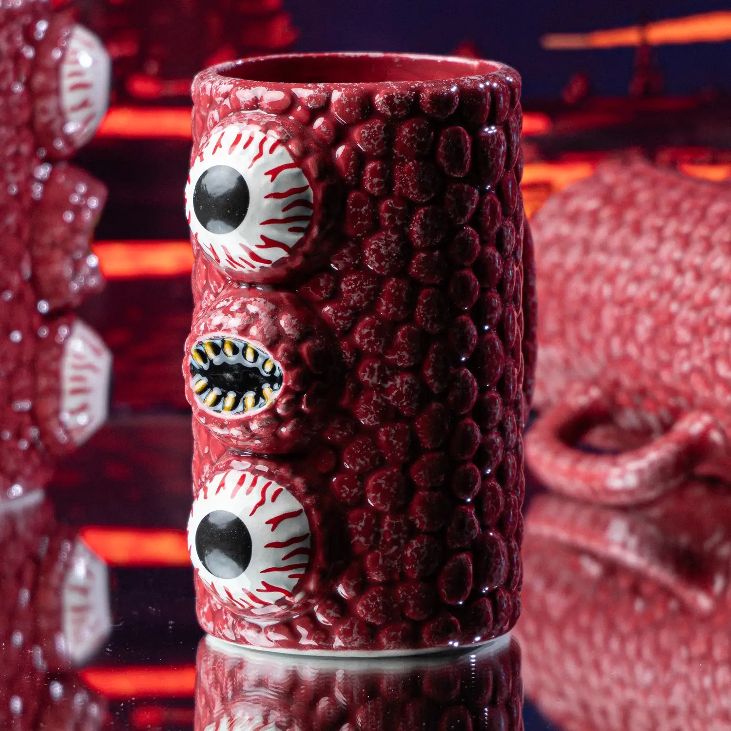 Red textured Wall of Flesh mug with eye and mouth designs on a reflective surface. Wall of Flesh Mug from Terraria.